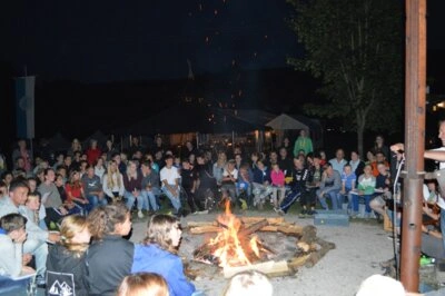 Ein Bild vom Jugendzeltlager bei dem um ein Lagerfeuer herum im Kreis gesessen wird.